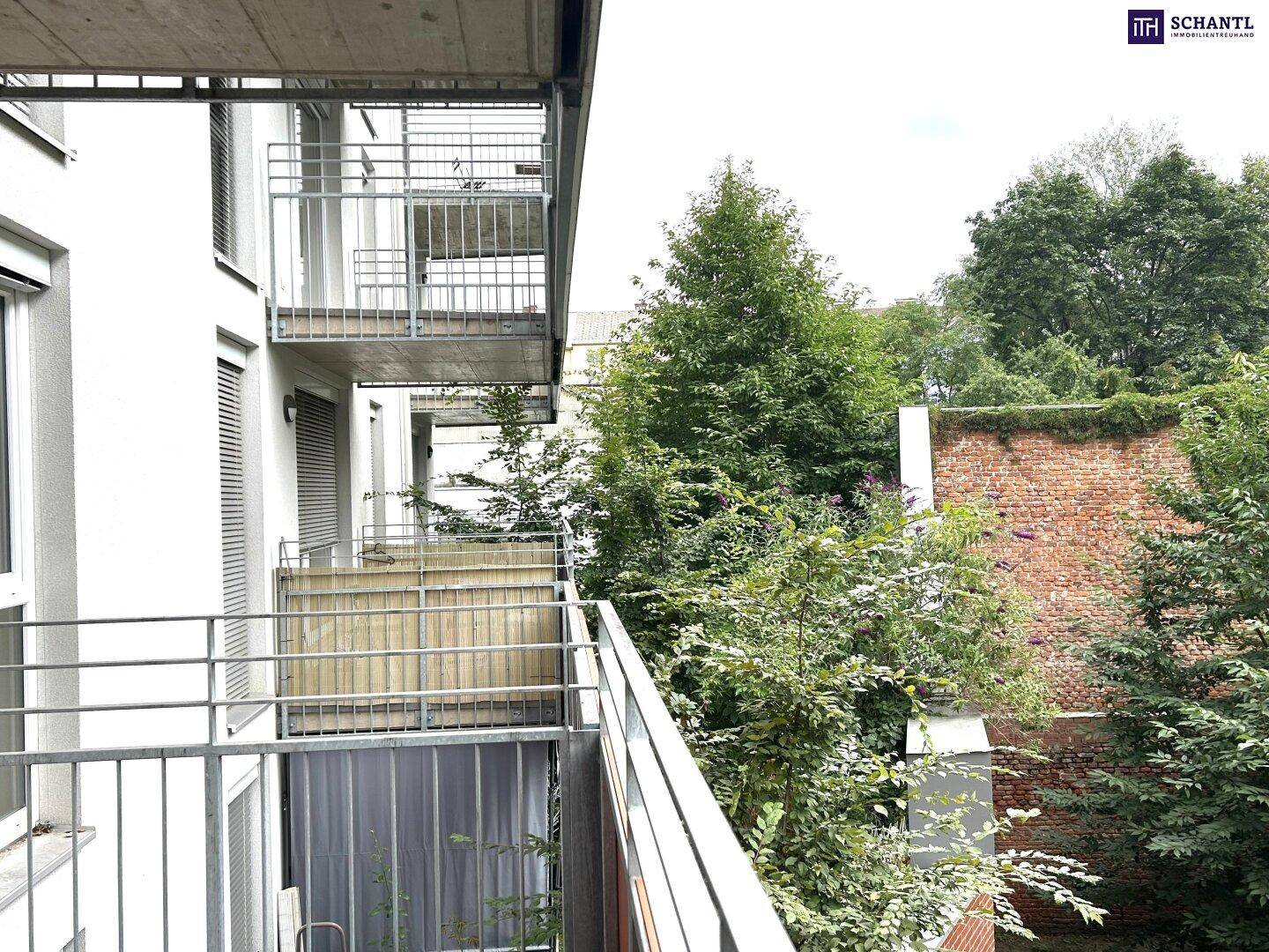 Mehrere Balkone an der Gebäudefassade mit Blick auf Bäume und eine alte Ziegelmauer.