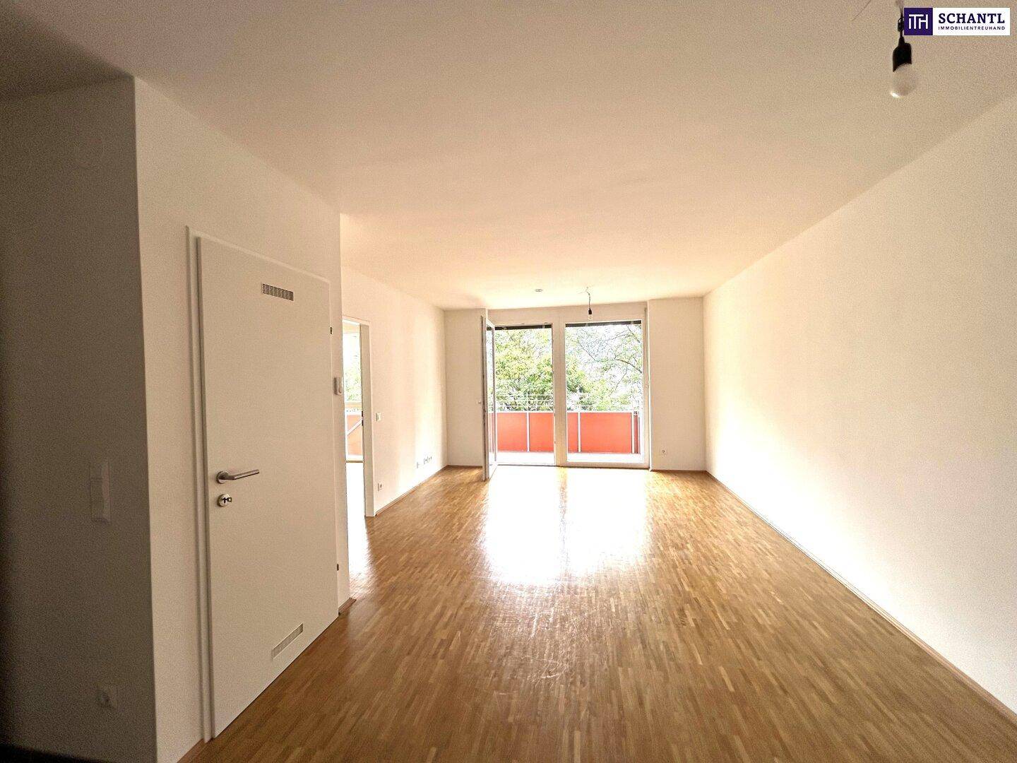 Heller Wohnbereich mit Parkettboden und Zugang zum Balkon, der viel Tageslicht hereinlässt.