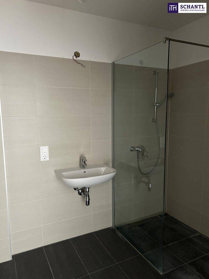 Modernes Badezimmer mit begehbarer Dusche, Waschbecken und hellen Fliesen an Wänden und Boden.