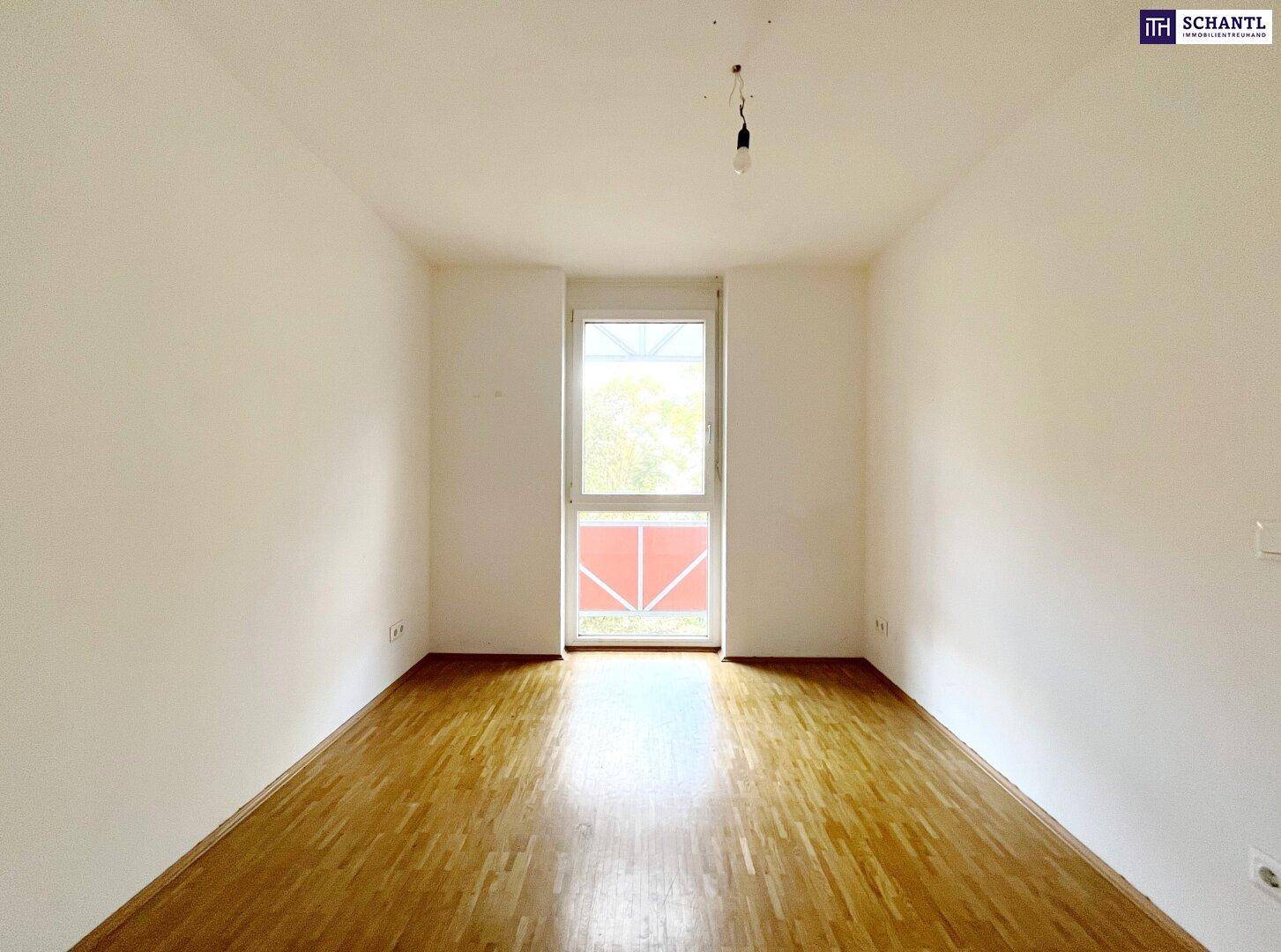 Helles Schlafzimmer mit Parkettboden und großem Fenster, das viel Tageslicht hereinlässt.