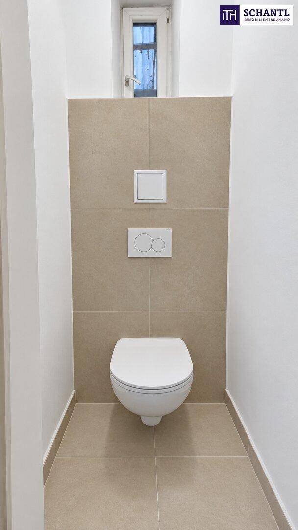 Separates WC mit Wand-WC, beigen Fliesen und kleinem Fenster für Belüftung.