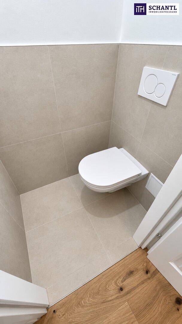Separates WC mit wandhängender Toilette und modernen Fliesen, zugänglich vom Holzbodenbereich.