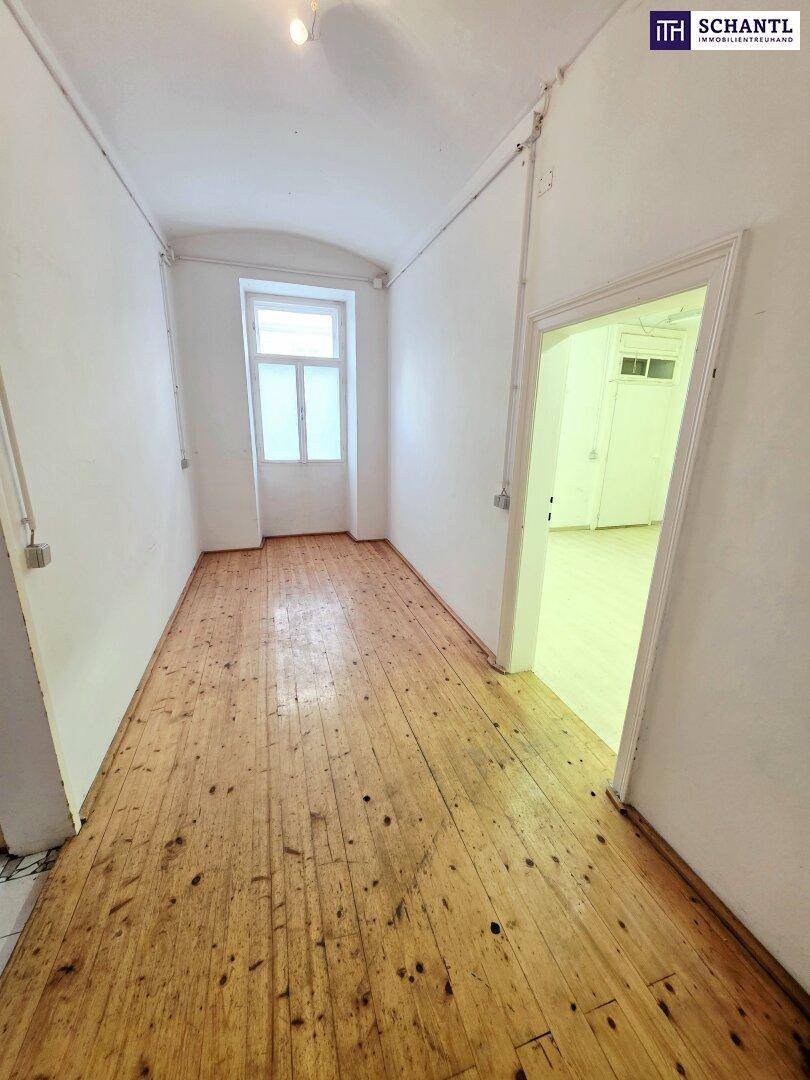 Langer, schmaler Flur mit rustikalem Holzplankenboden und einem Fenster am Ende, das Tageslicht hereinlässt.