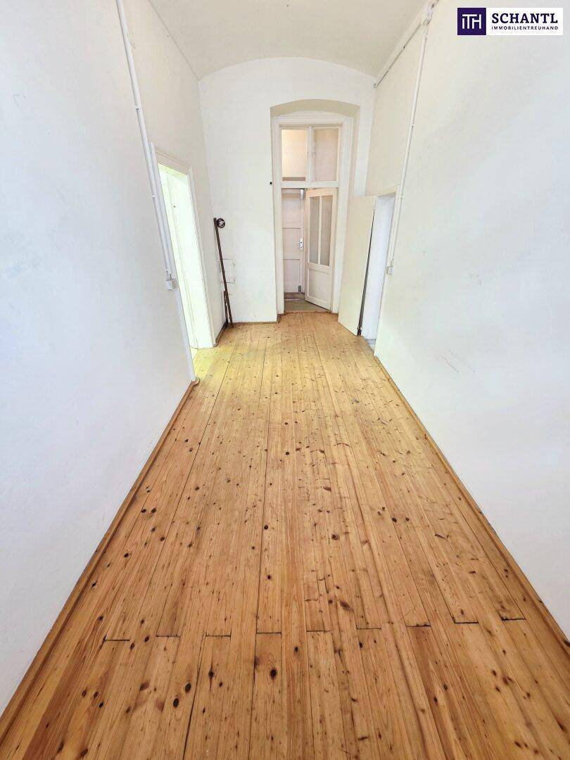 Langer, heller Flur mit rustikalem Holzplankenboden und einem großen Fenster am Ende, das viel Licht spendet.