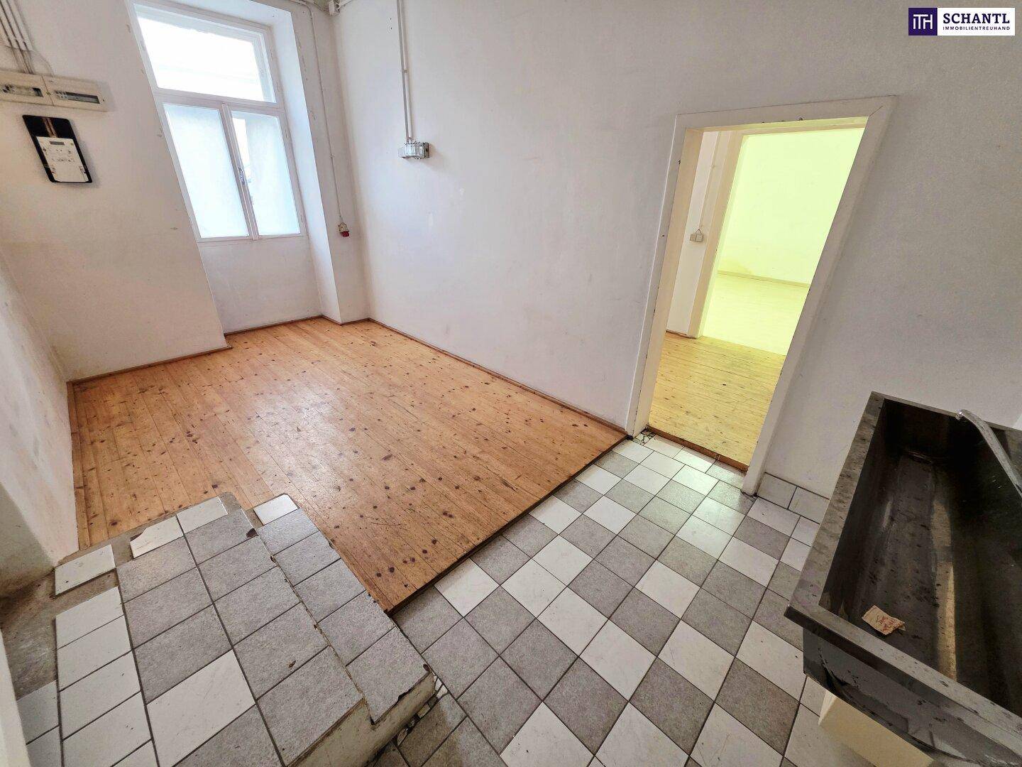Bereich mit gemusterten Fliesen und Holzplankenboden, verbunden durch Stufen, mit einem Fenster für Tageslicht.