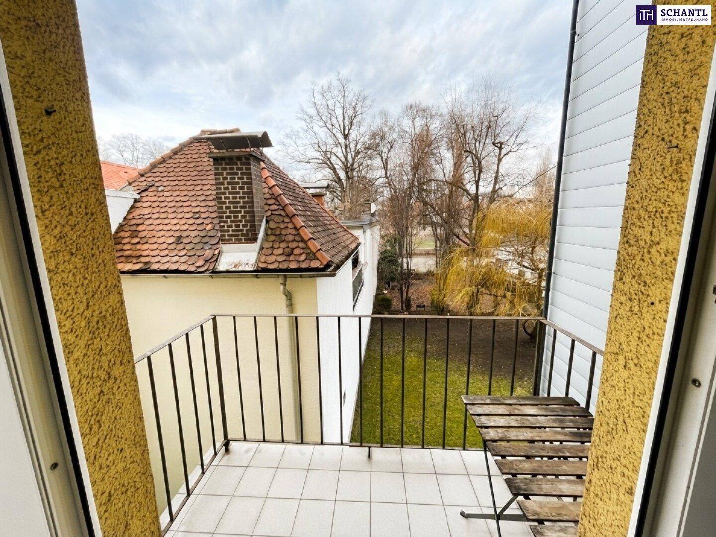 Kleiner Balkon mit Fliesenboden und Holztisch, bietet einen Blick ins Grüne.