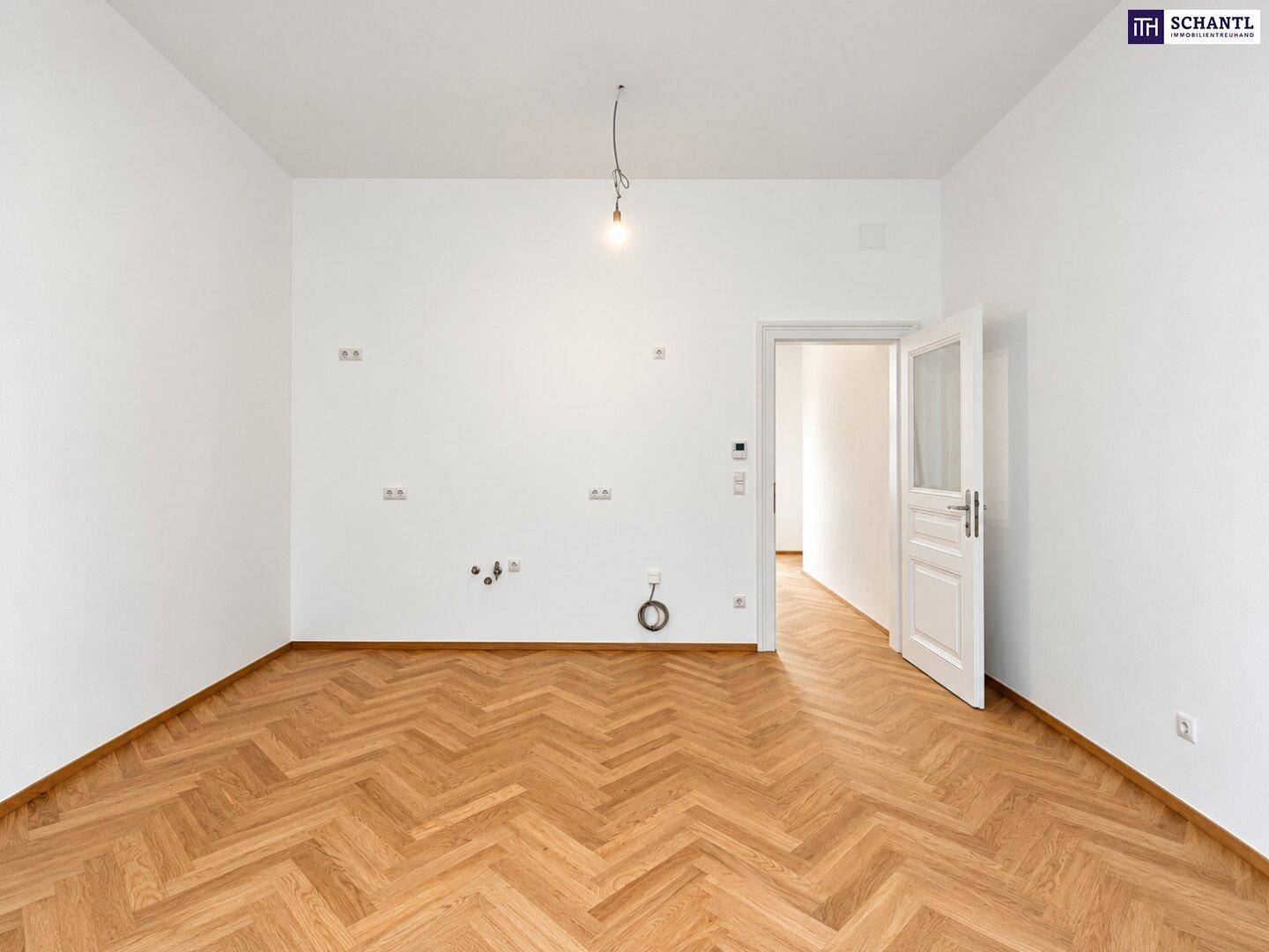 Leerer Raum mit Fischgrätparkett und Anschlüssen für eine Küche, bereit für den Einbau.