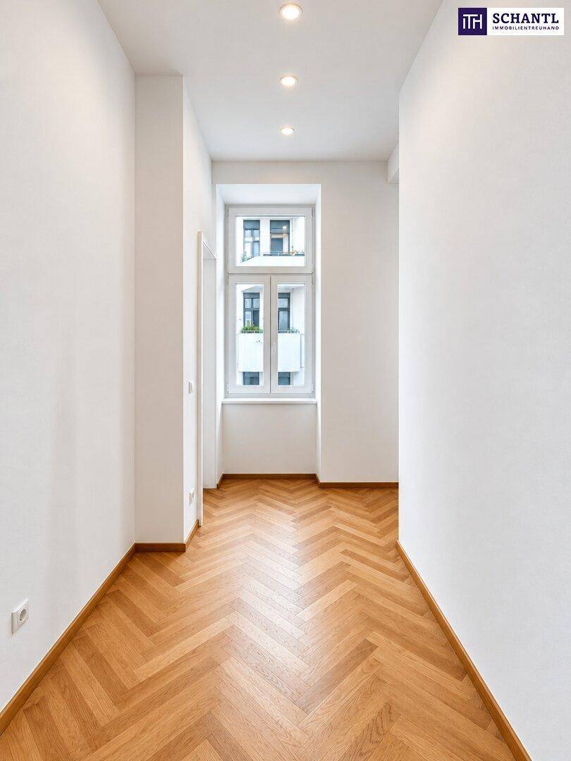 Heller Flur mit Fischgrätparkett und einem Fenster am Ende, ausgestattet mit Deckenspots.