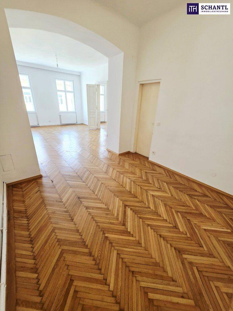 Großzügiger Raum mit Fischgrätparkett und offenem Durchgang zu einem weiteren Zimmer.