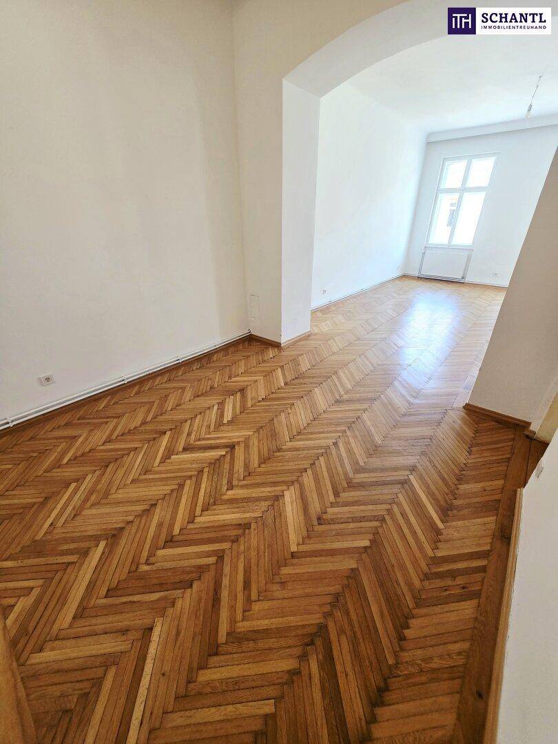 Langer Raum mit glänzendem Fischgrätparkett und weiß gestrichenen Wänden.