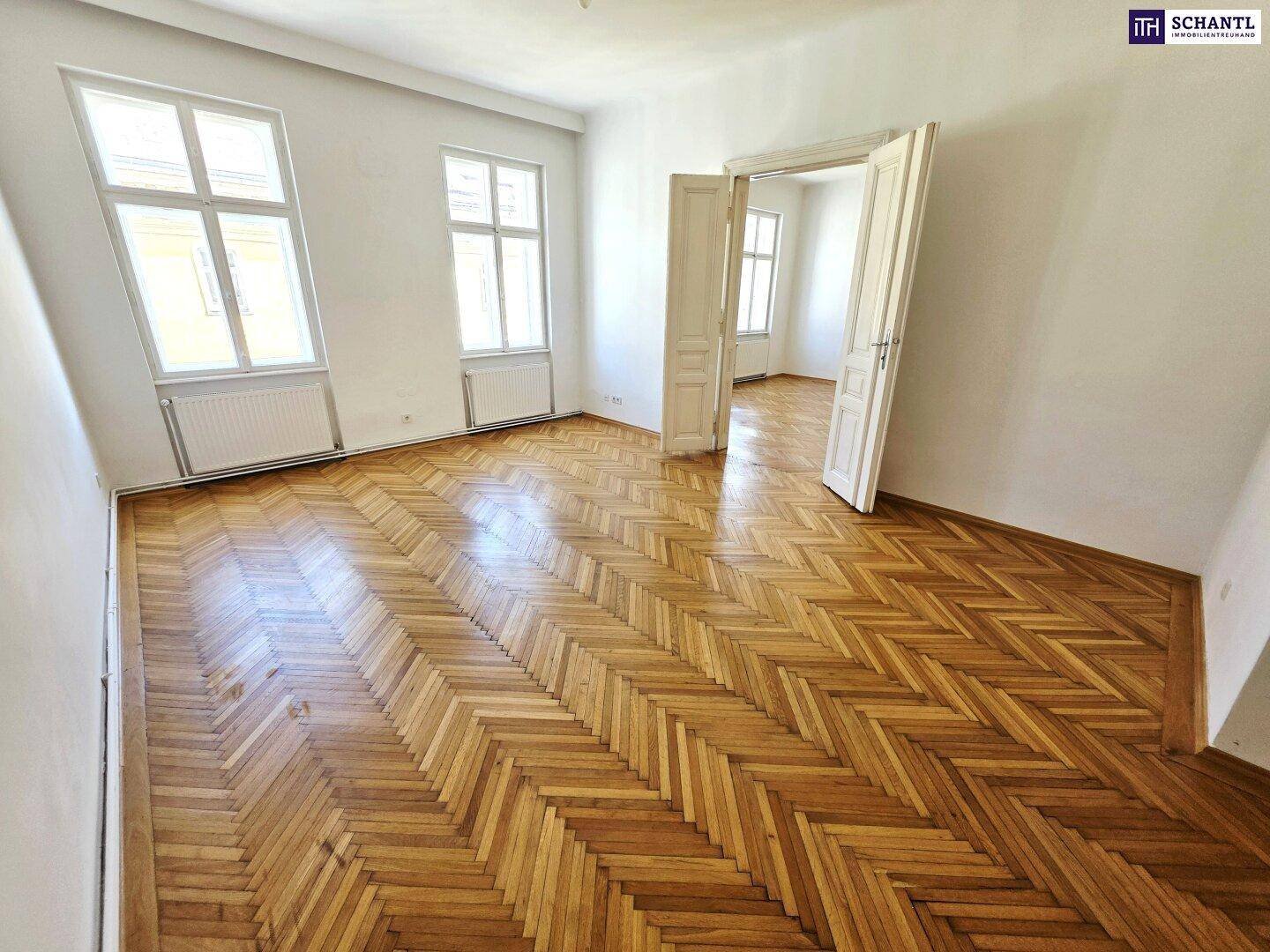 Geräumiges Zimmer mit klassischem Fischgrätparkett und großen Fenstern, ideal für Wohnzwecke.