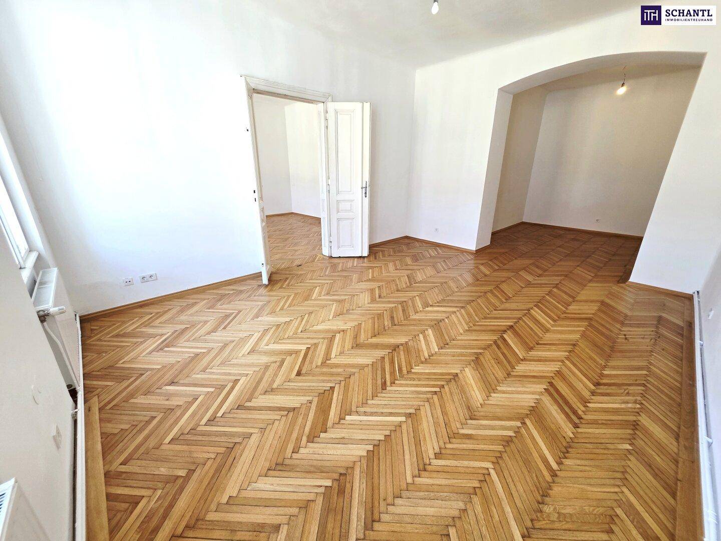 Heller Raum mit Fischgrätparkett und einem Bogen, der zu einem weiteren Bereich führt.