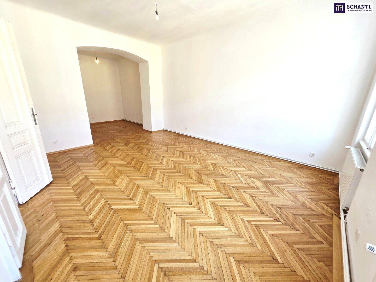 Leeres Zimmer mit hellem Fischgrätparkett und einem Durchgang zu einem angrenzenden Raum.