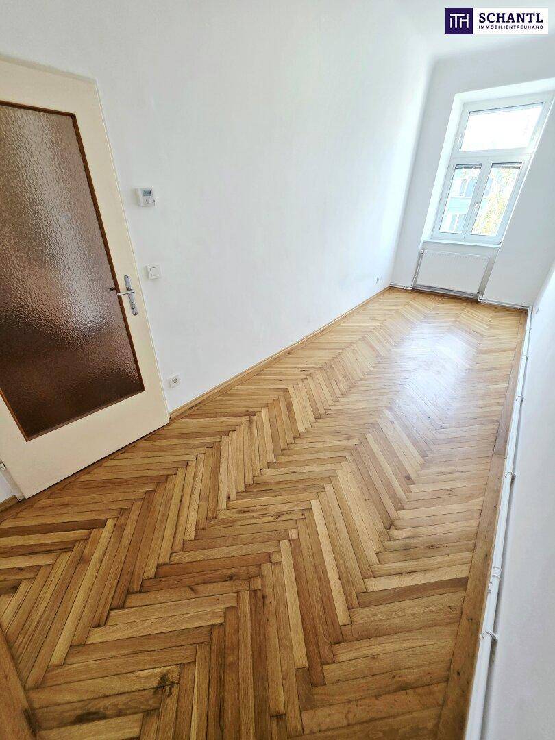 Schmaler Raum mit Fischgrätparkett und einem Fenster, das Tageslicht hereinlässt.