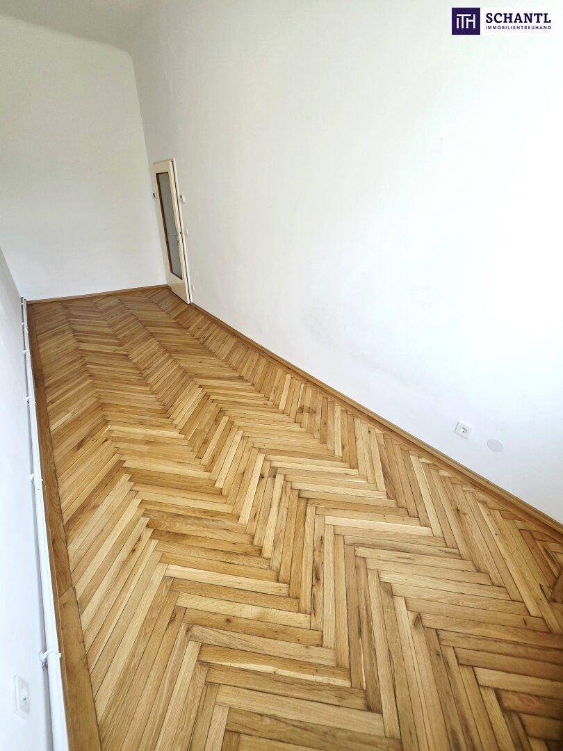 Langer, heller Raum mit klassischem Fischgrätparkett und weißen Wänden.