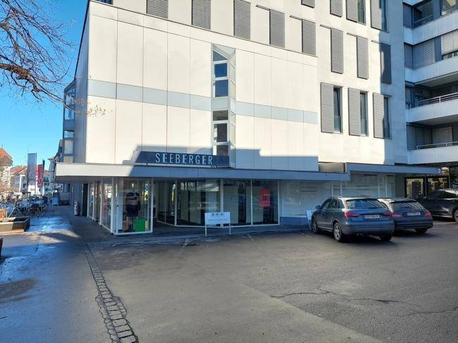 Ansicht der Geschäftsfassade mit großen Schaufenstern und angrenzendem Parkplatzbereich.
