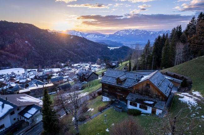 Atemberaubender Sonnenuntergang über den Bergen mit Blick auf das traditionelle Holzhaus und das Tal.