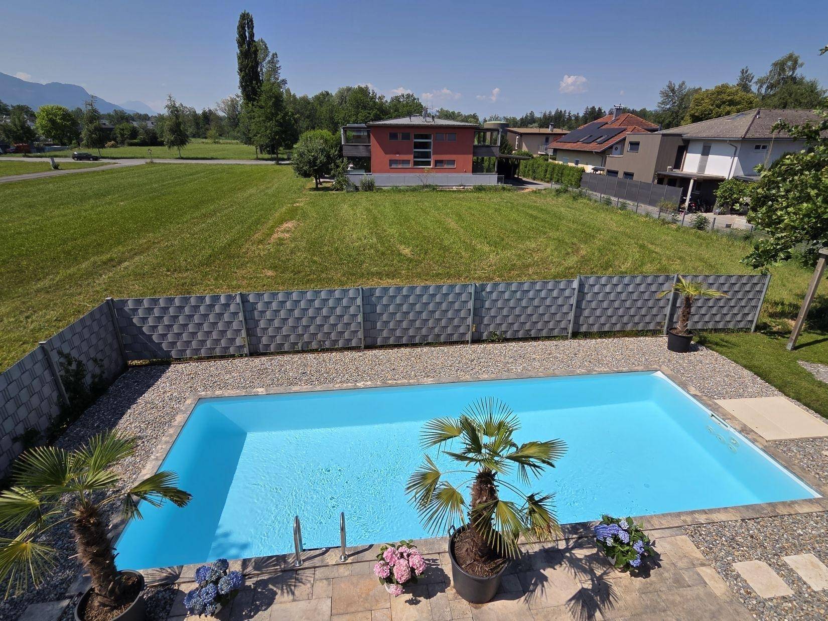 Panoramablick auf den Poolbereich und die weite grüne Landschaft mit Bergen im Hintergrund.