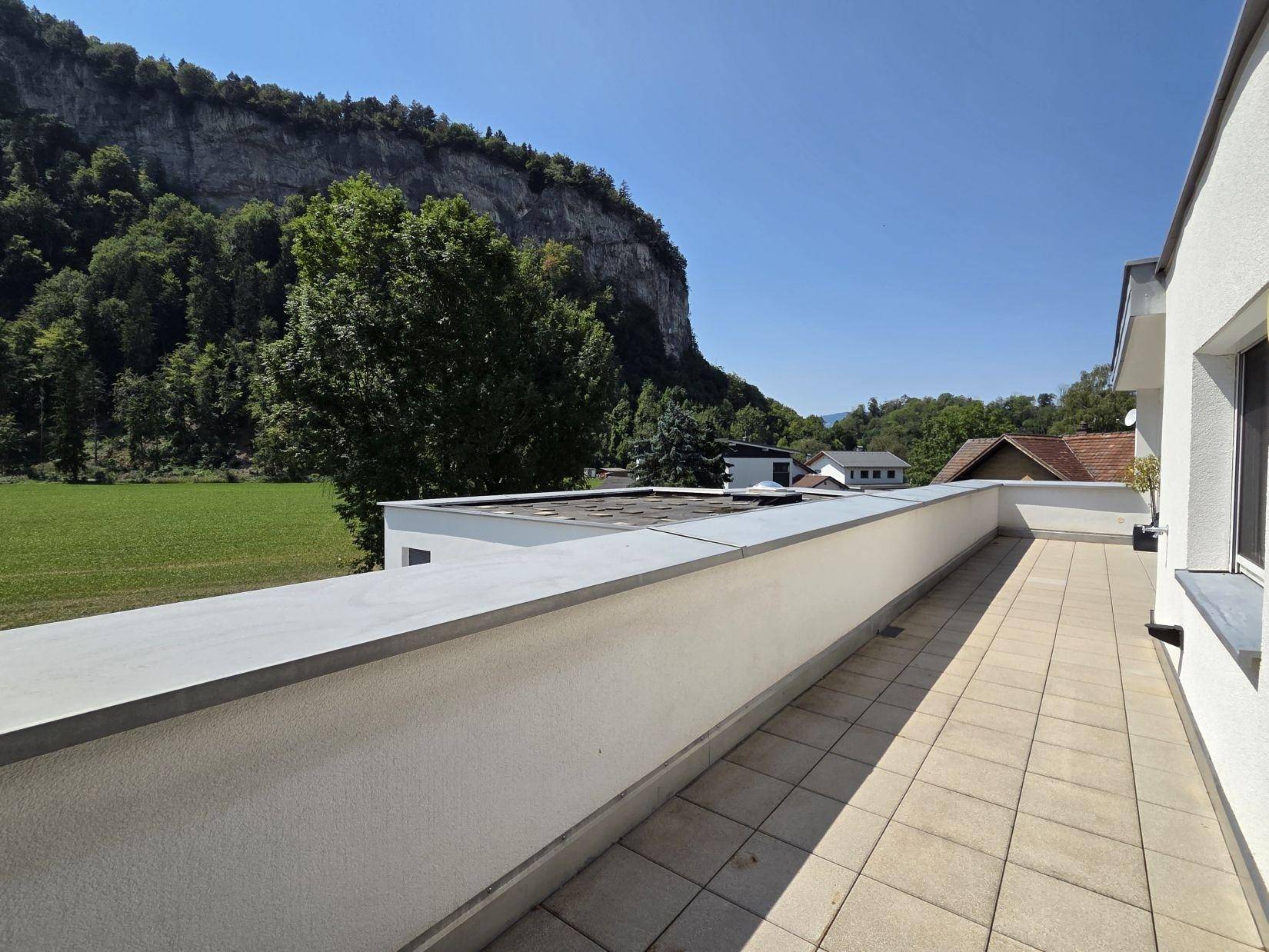 Weitläufiger Blick von der Terrasse auf grüne Felder und eine beeindruckende Felswand.
