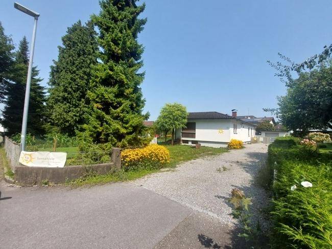 Zufahrt zum Grundstück mit Kiesweg, hohen Bäumen und einem Gartenschule-Schild.
