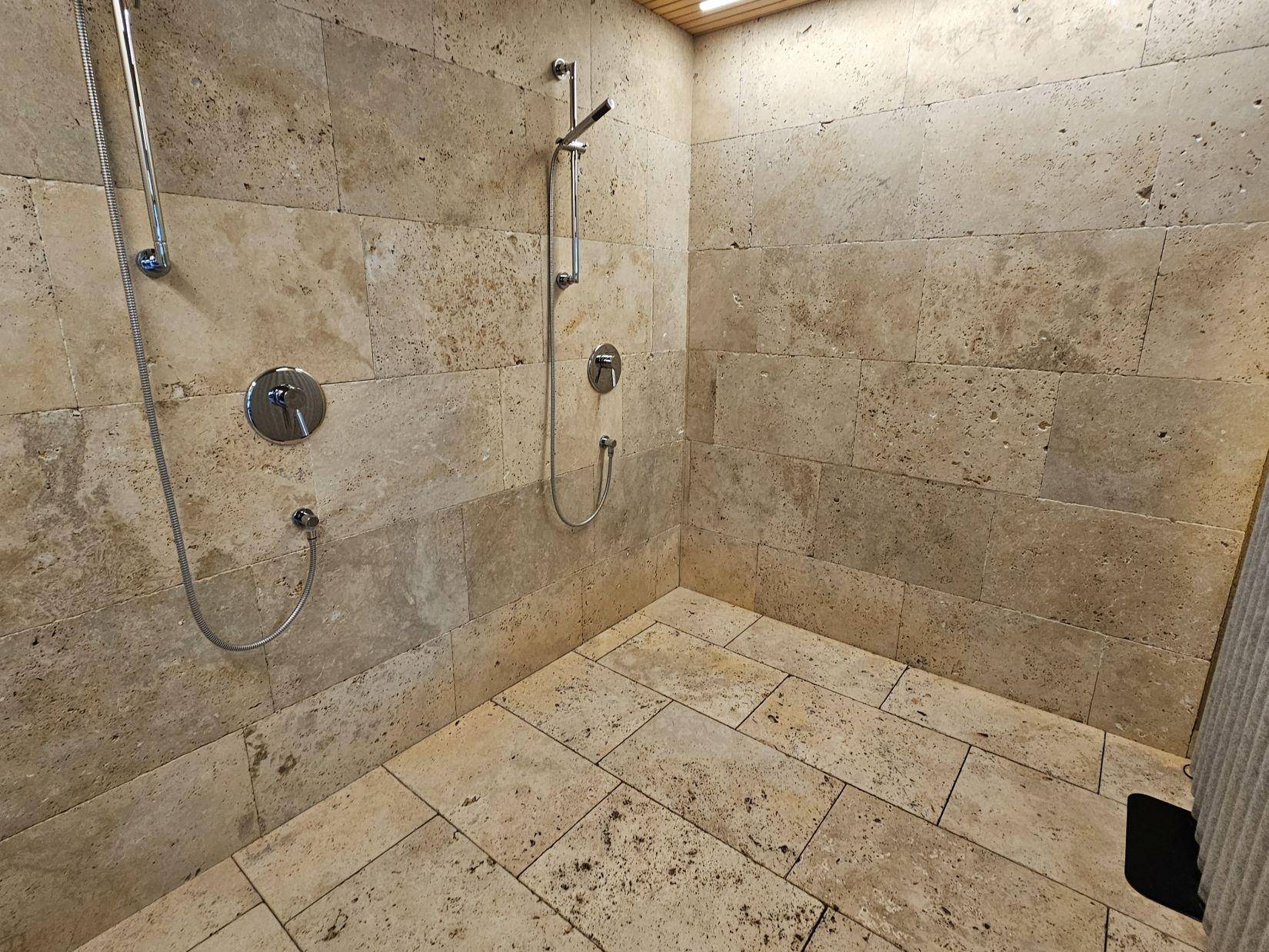 Moderne begehbare Dusche mit beigefarbenen Fliesen und zwei Duschköpfen für Komfort.