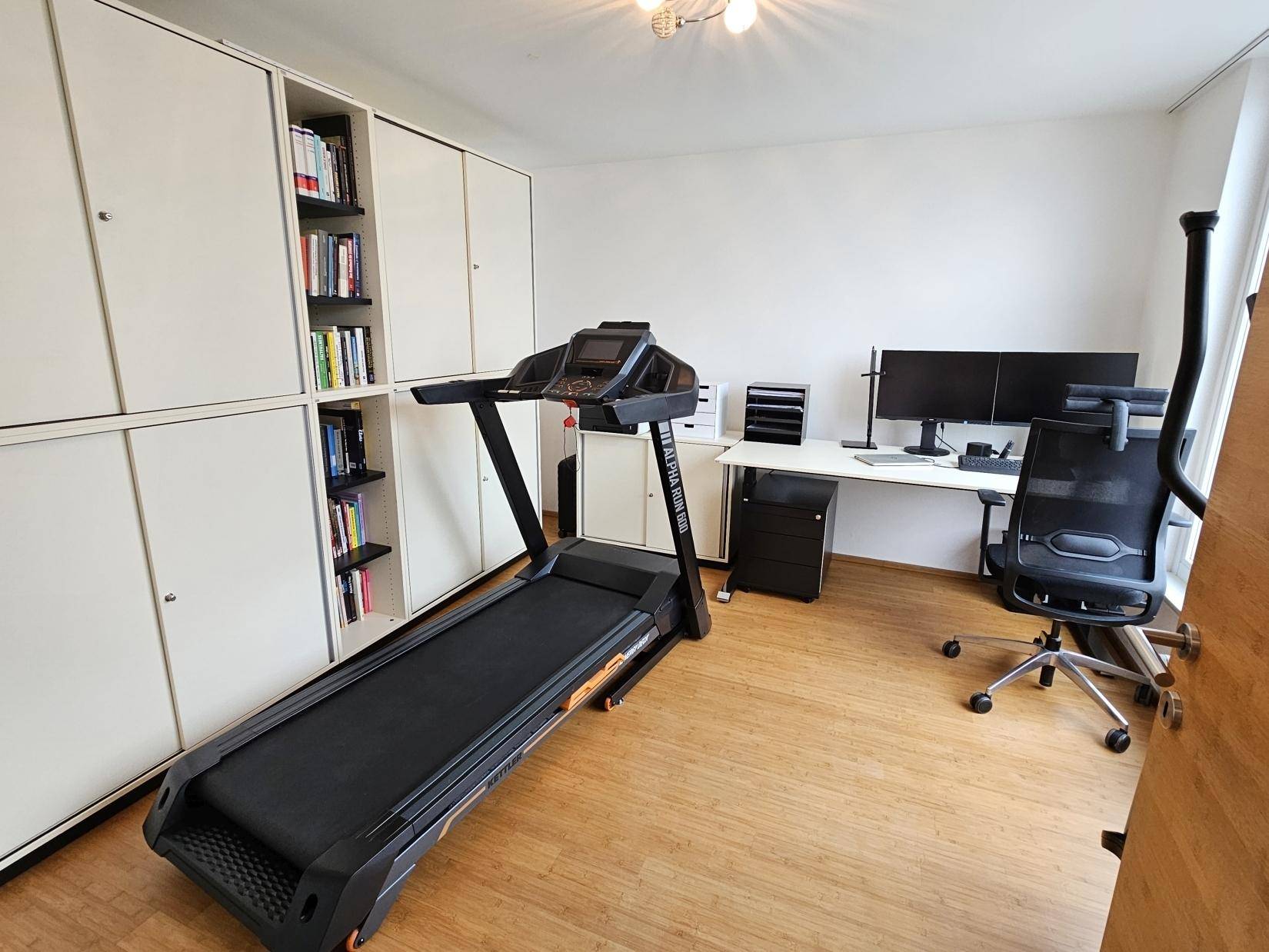 Arbeitszimmer mit Laufband, Schreibtisch und Einbauschränken, ideal für Home-Office und Fitness.