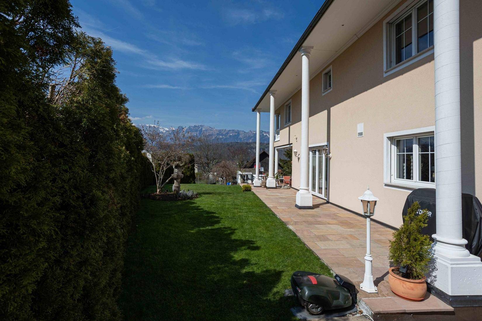 Langer Gartenbereich entlang der Villa mit Rasen und Hecke, ideal für Entspannung.