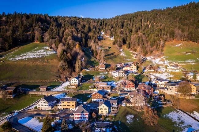 Panoramablick auf das malerische Bergdorf, umgeben von Wäldern und schneebedeckten Hängen.