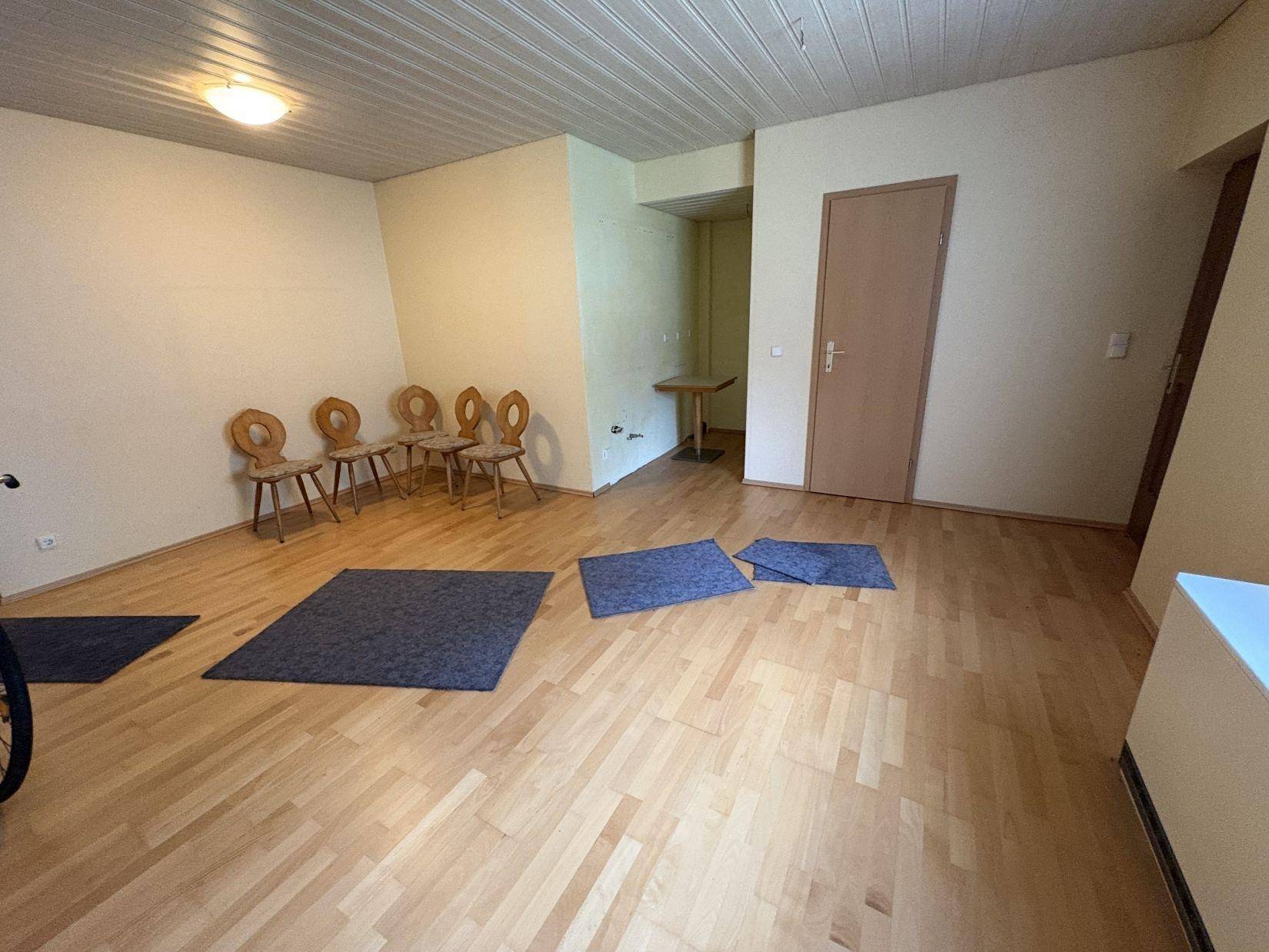 Geräumiger Raum mit Holzparkettboden, Holzdecke und mehreren Holzstühlen, ideal als Büro.