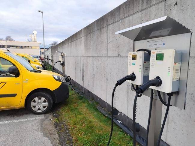 Mehrere Elektrofahrzeug-Ladestationen entlang einer Betonwand mit geparkten Lieferwagen.