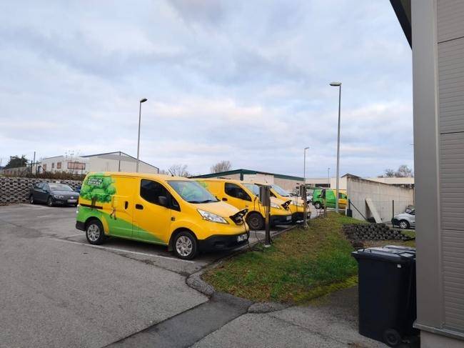 Reihe von Elektrofahrzeug-Ladestationen mit geparkten Lieferwagen auf dem Parkplatz.