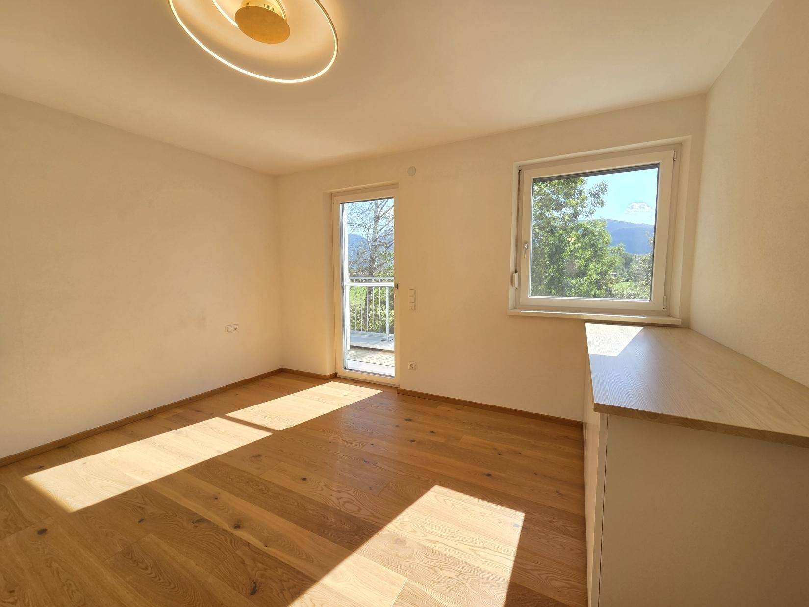 Sonniges Schlafzimmer mit Eichenparkett, großem Fenster und Zugang zu einem französischen Balkon.