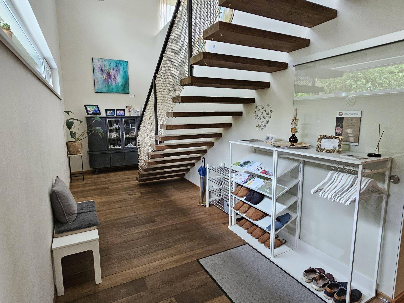 Eingangsbereich mit offener Holztreppe, Garderobe und Schuhregal, hell und einladend gestaltet.