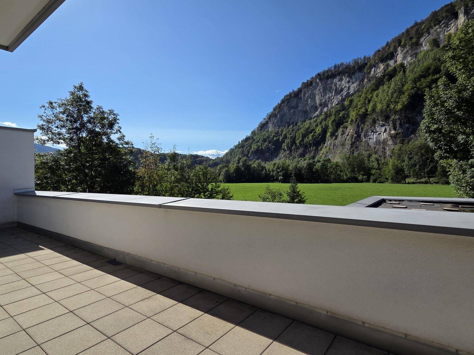 Helle Terrasse mit Fliesenboden und freiem Blick auf die umliegende Natur und Berge.
