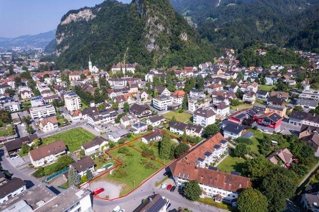 Luftaufnahme einer Stadt mit Bergen und einem rot umrandeten Grundstück im Zentrum.