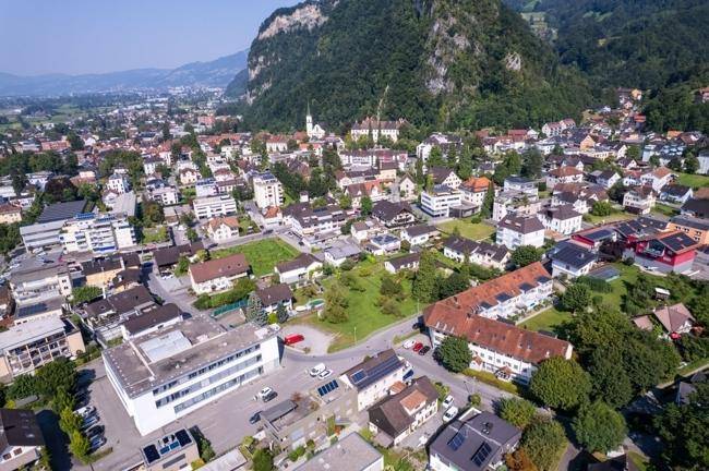 Panoramische Luftaufnahme einer Stadtlandschaft mit grünen Bergen im Hintergrund.