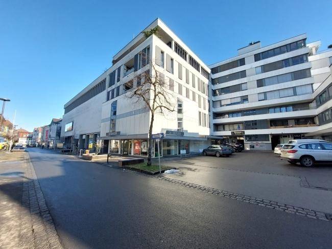 Weitwinkelansicht des modernen Geschäftsgebäudes an einer Straße mit parkenden Autos unter blauem Himmel.