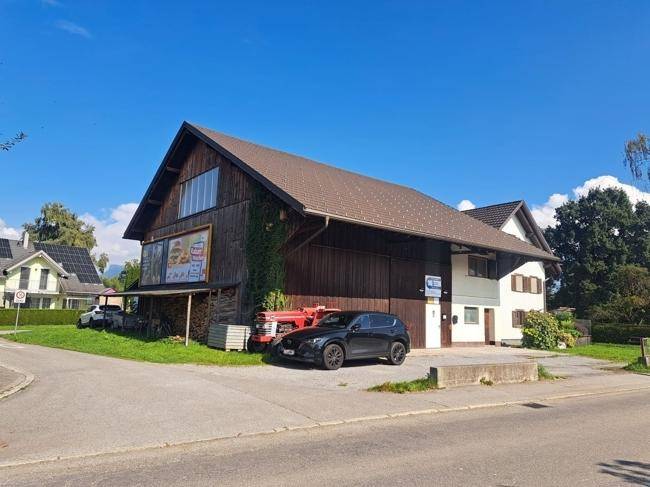 Gesamtansicht des Gebäudes mit Holzfassade, Satteldach und Parkplätzen an der Straßenecke.