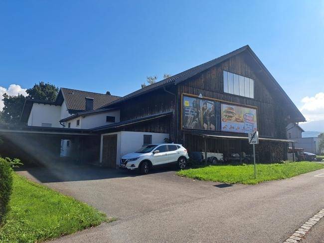 Großes Gebäude mit Holzfassade, Carport und Werbetafeln an einer ländlichen Straße gelegen.