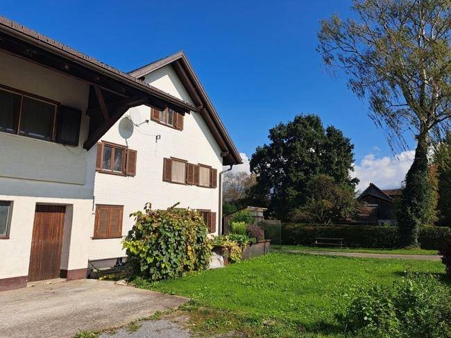 Gepflegter Gartenbereich neben dem Haus mit Rasenfläche und hohen Bäumen an einem sonnigen Tag.