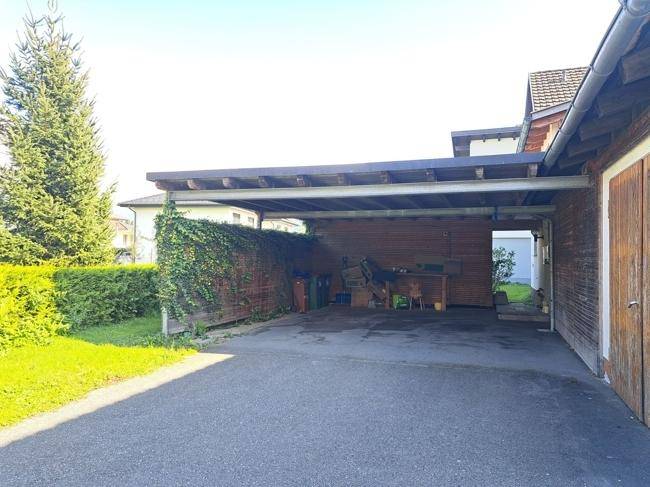Überdachter Carport-Bereich mit Rankpflanzen und angrenzender Grünfläche an einem sonnigen Tag.
