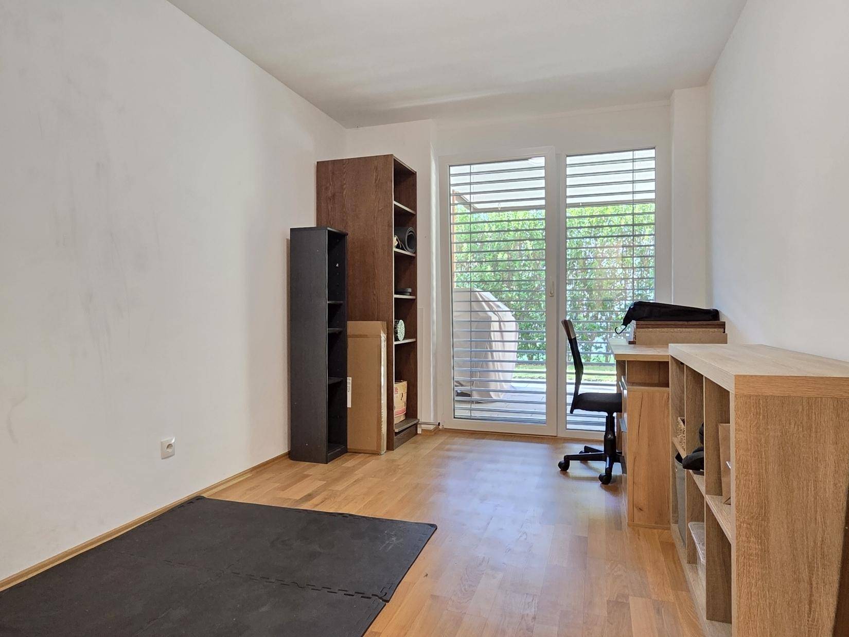 Funktionales Arbeitszimmer mit Schreibtisch, Regalen und Zugang zu einem Außenbereich.