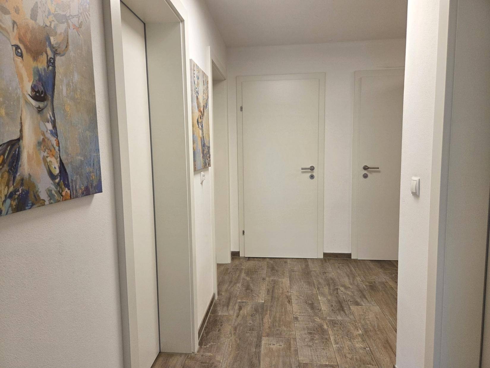 Heller Flur mit Holzboden und weißen Türen, geschmückt mit moderner Kunst.