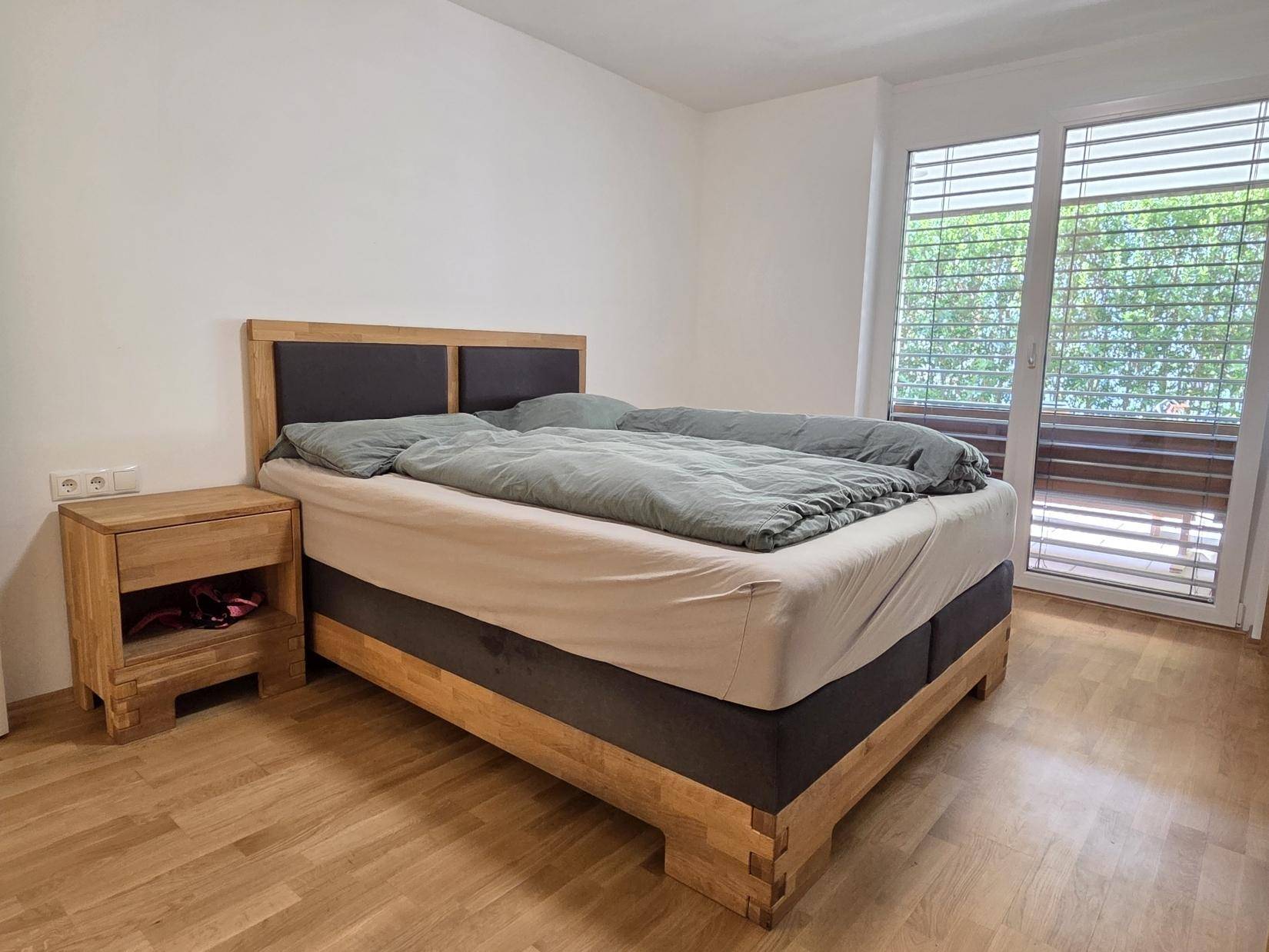 Schlafzimmer mit Holzbett, Nachttisch und direktem Zugang zu einem Außenbereich.