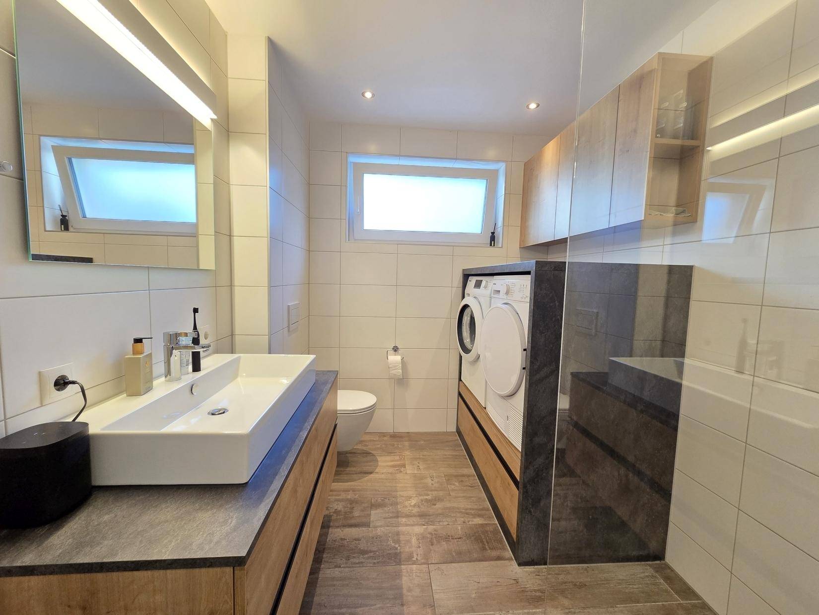 Modernes Badezimmer mit Doppelwaschbecken, Toilette und integrierter Waschmaschine/Trockner.