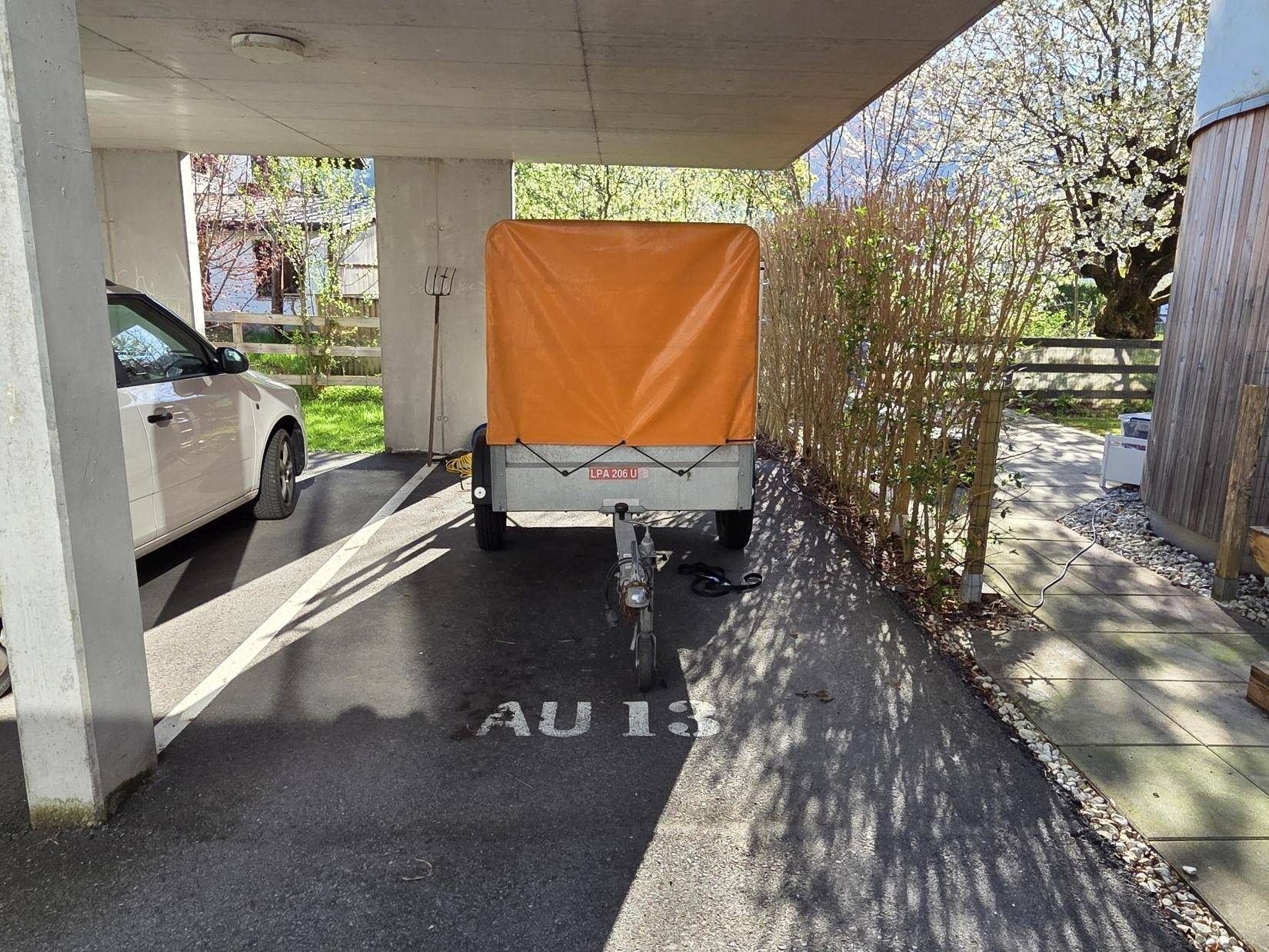 Überdachter Parkplatz unter einem Carport mit einem Anhänger und markierter Stellfläche.