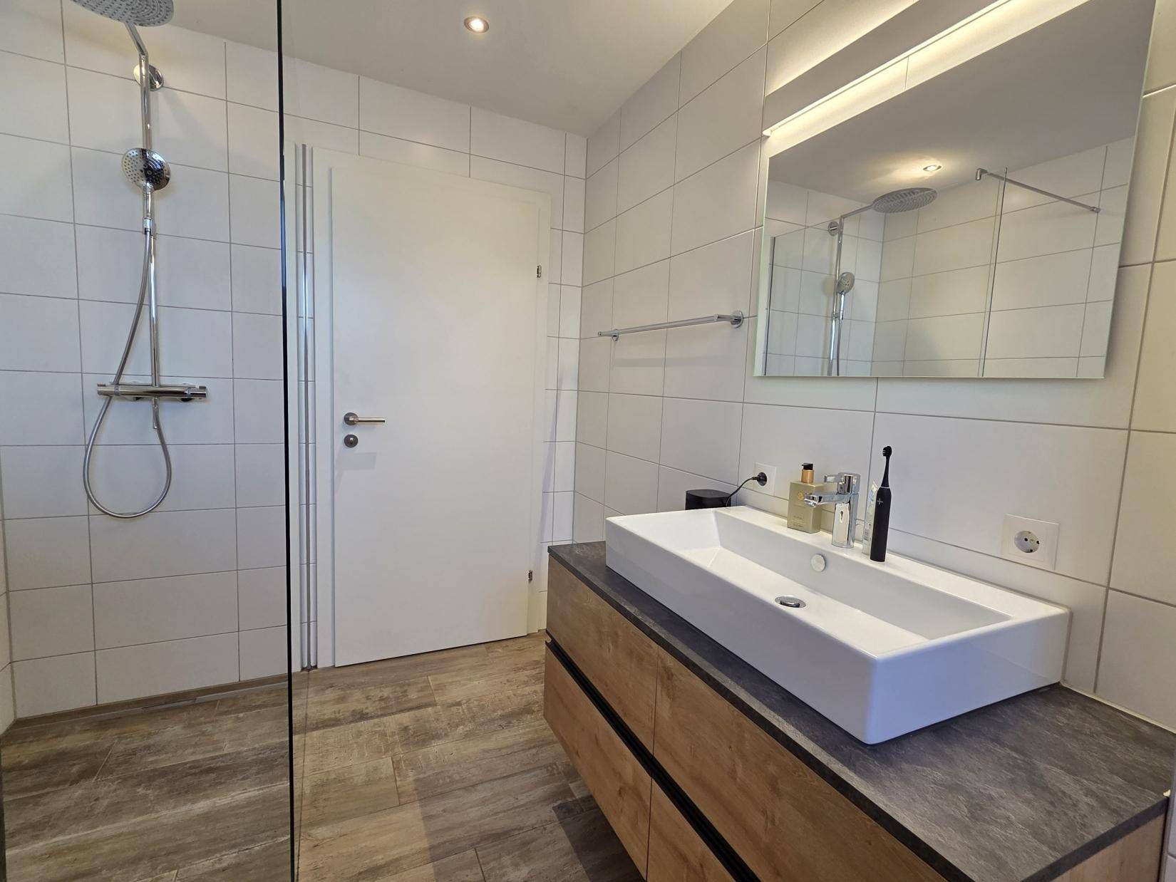 Helles Badezimmer mit begehbarer Dusche, modernem Waschtisch und beleuchtetem Spiegel.