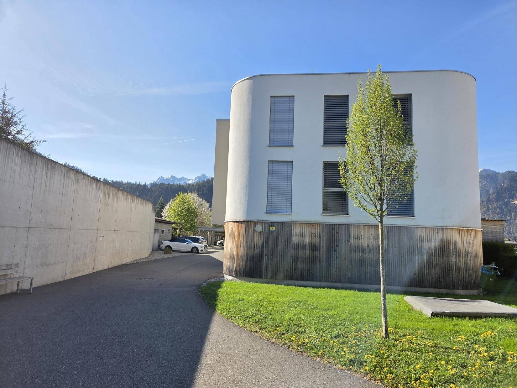 Modernes Wohngebäude mit abgerundeter Fassade, Holzverkleidung und Grünfläche.