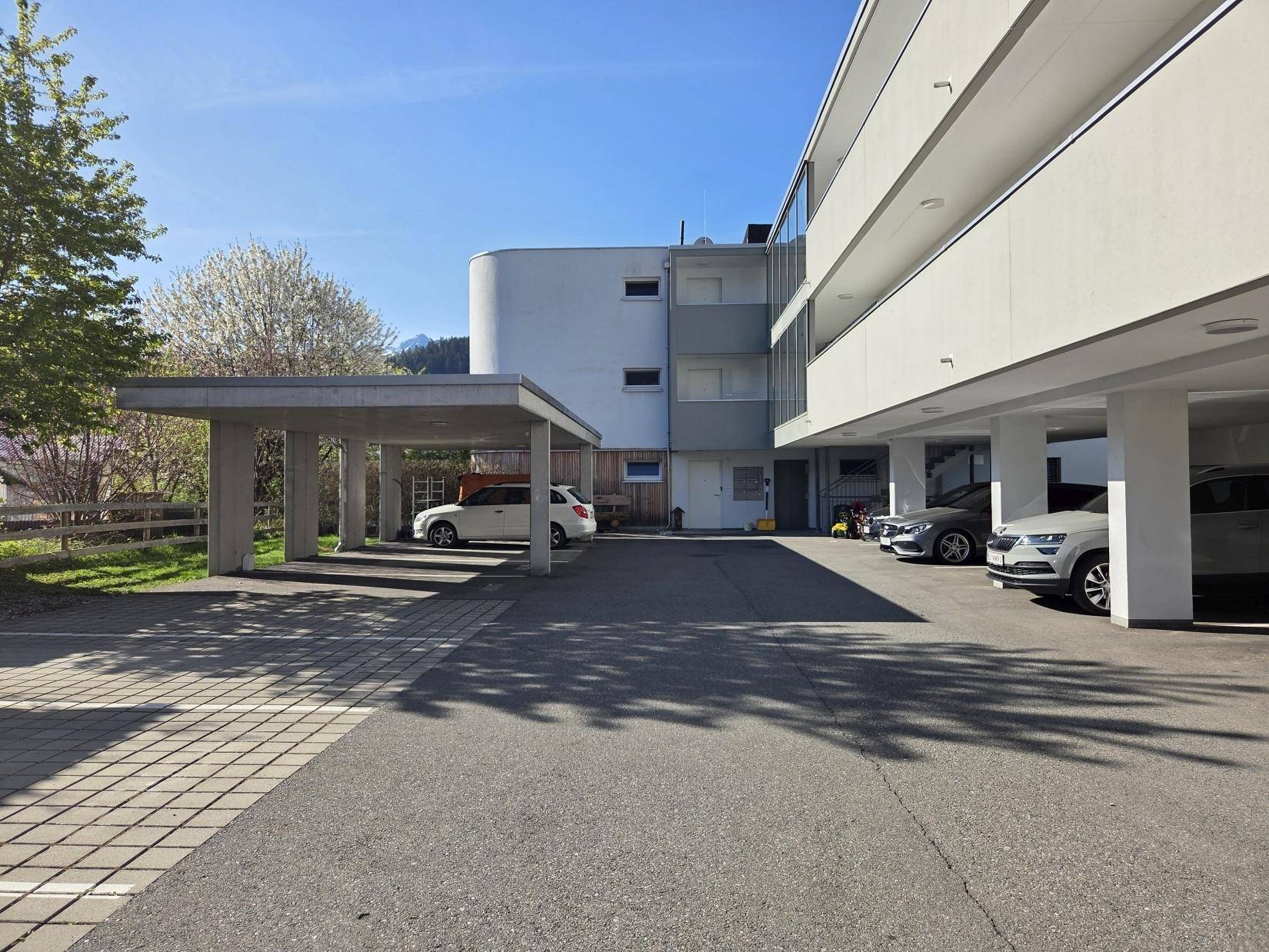 Moderne Wohnanlage mit Carports und Außenparkplätzen unter blauem Himmel.