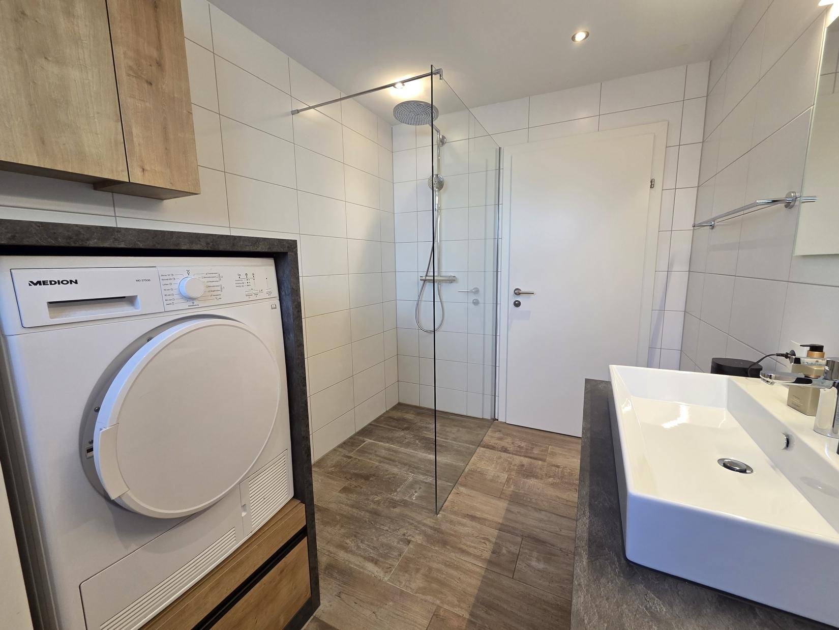 Badezimmer mit geräumiger begehbarer Dusche und praktischer Waschmaschine/Trockner-Kombination.